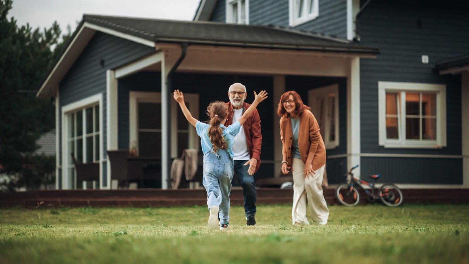 A grandfather and grandmother in their late sixties greeting their grandchild in the backyard of their home, warm and well